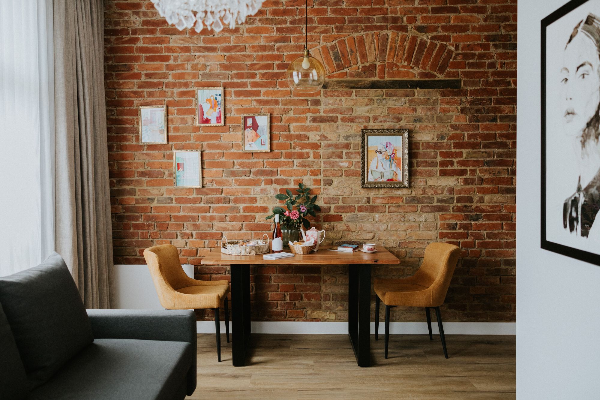 Kącik jadalny z drewnianym stołem, dwoma musztardowymi krzesłami, bukietem kwiatów i ceglaną ścianą w tle